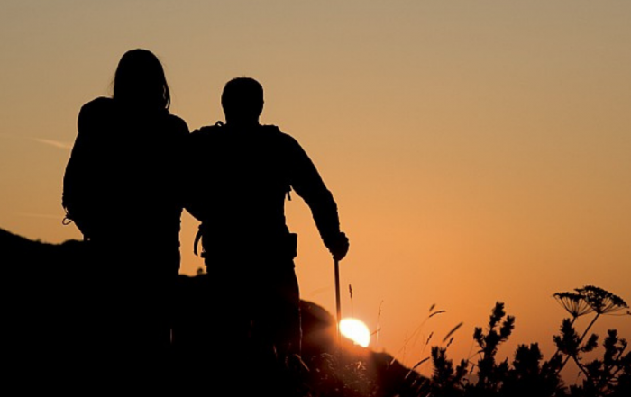 Silhouette of two people walking towards a sunset against an orange sky.